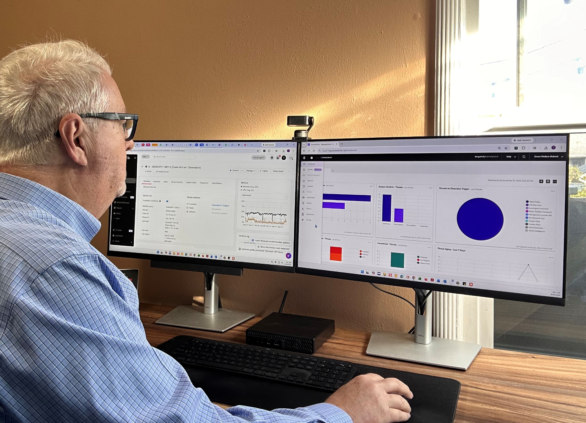 Owen Wollum working at dual monitors displaying technology management and security dashboards