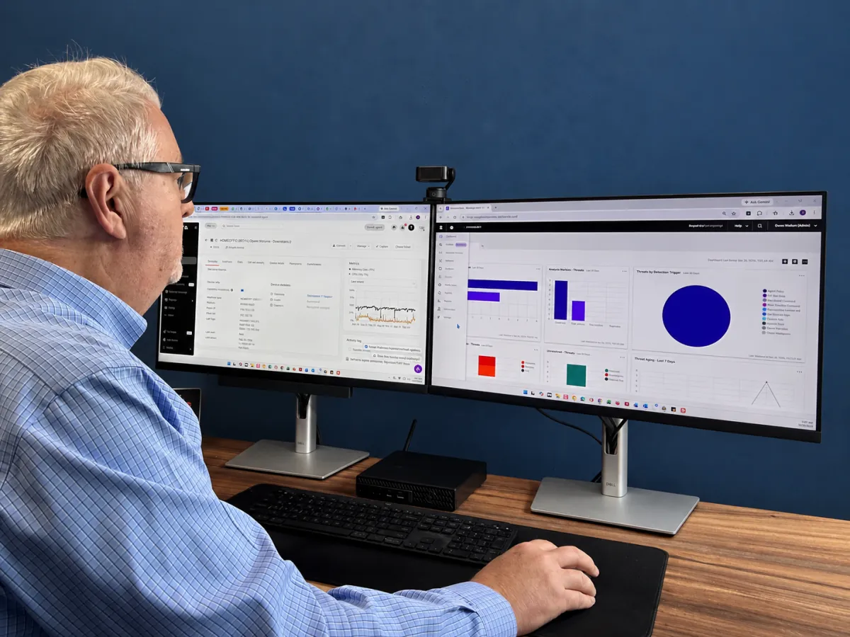 Owen Wollum working at dual monitors displaying technology management and security dashboards