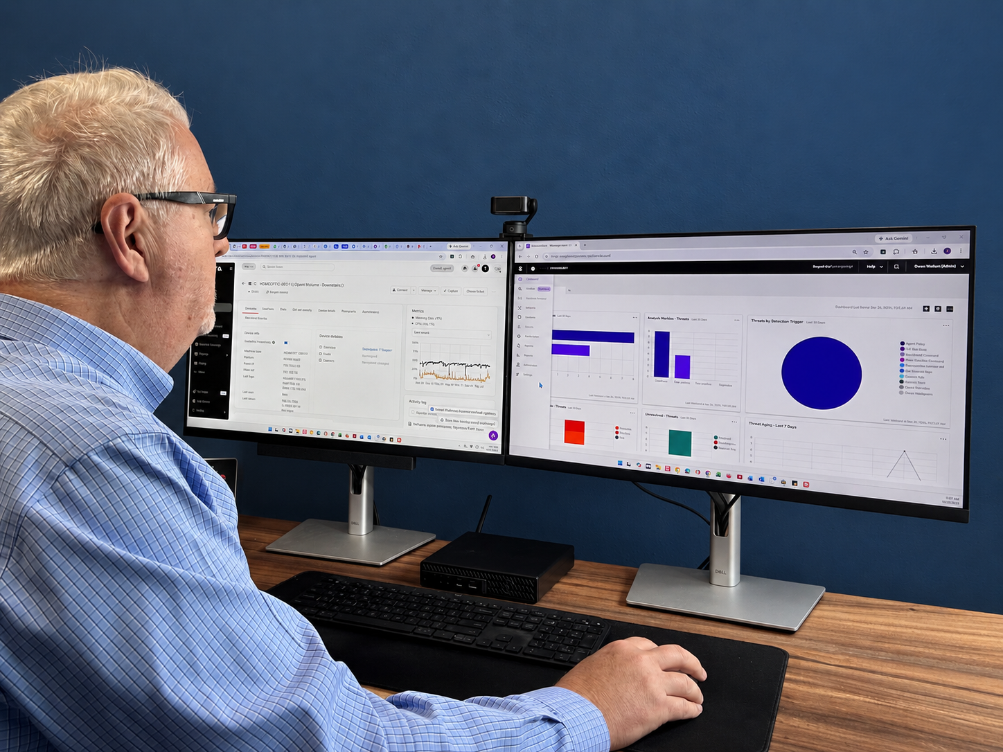 Owen Wollum working at dual monitors displaying technology management and security dashboards
